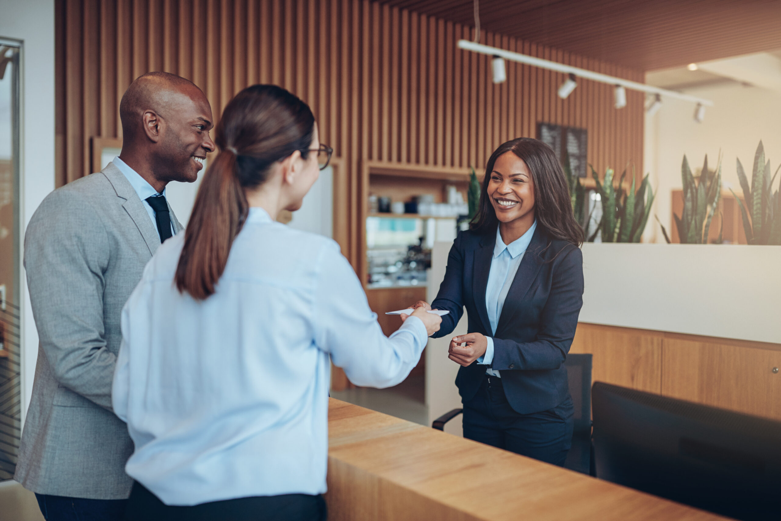 Two guests giving their reservation details to a smiling concierge while checking in together at the reception counter of a hotel